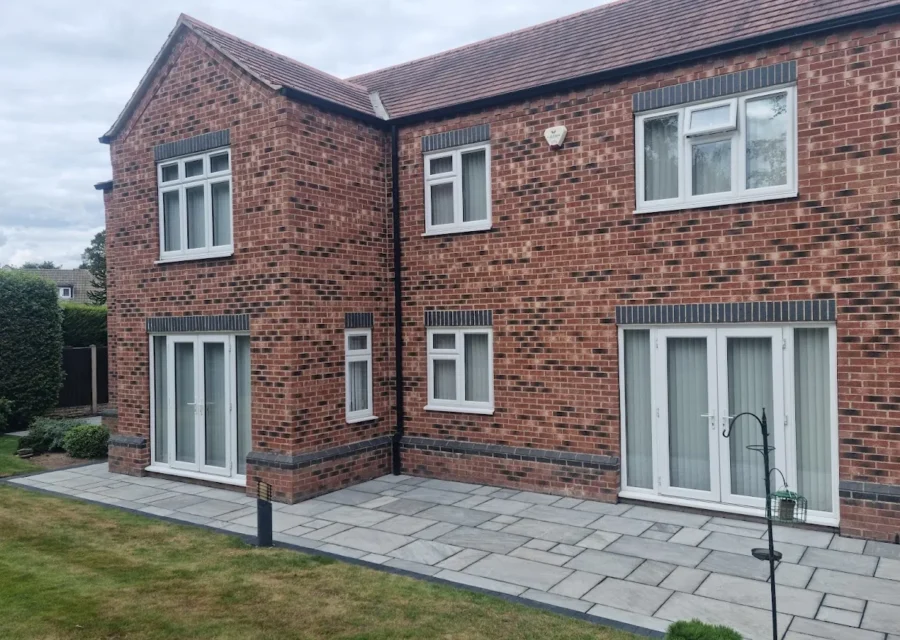 Grey Indian stone patio laid the full width of a red brick detached house