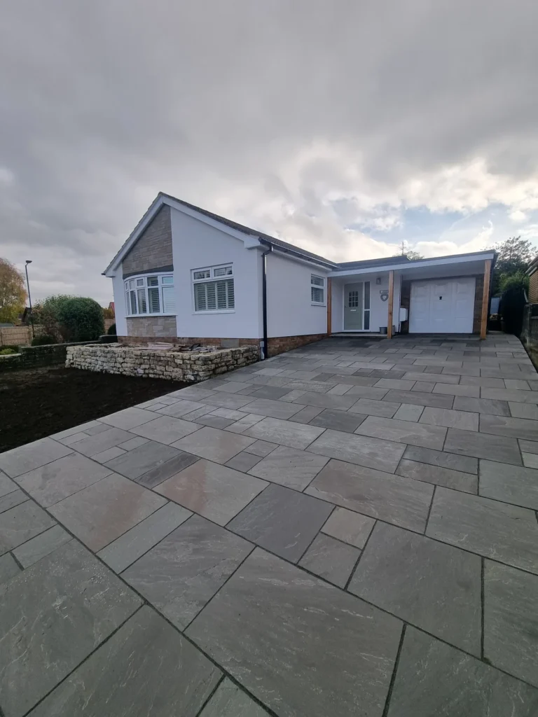 Wide grey sandstone paved driveway sweeping across the frontage of a white rendered bungalow with a walled border