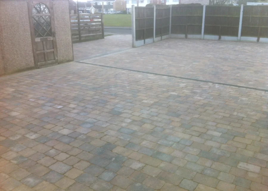 Large tumbled block paved parking area enclosed by concrete post and panel fencing