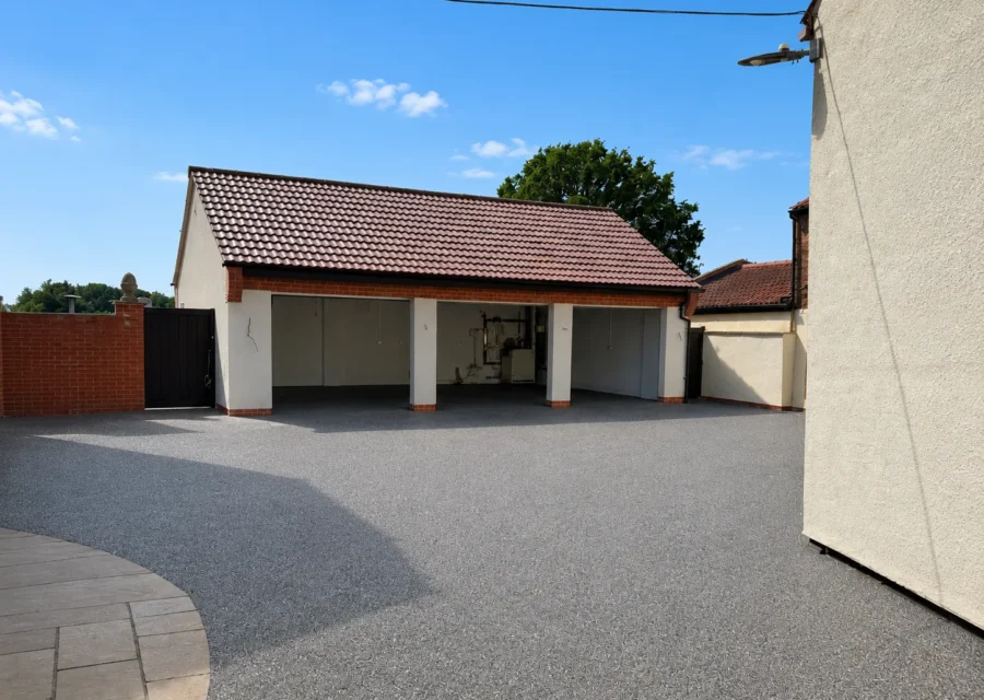 Pale resin bound driveway and turning area in front of an open fronted tiled garage block
