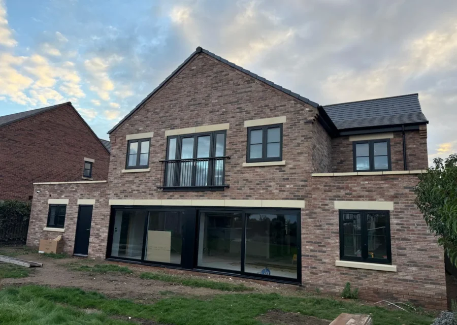 Newly built brick rear extension with wide black-framed glazed sliding doors across the back of a house